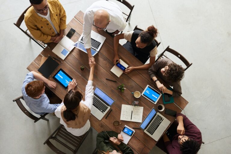 Group of diverse coworkers sitting around table with laptops.