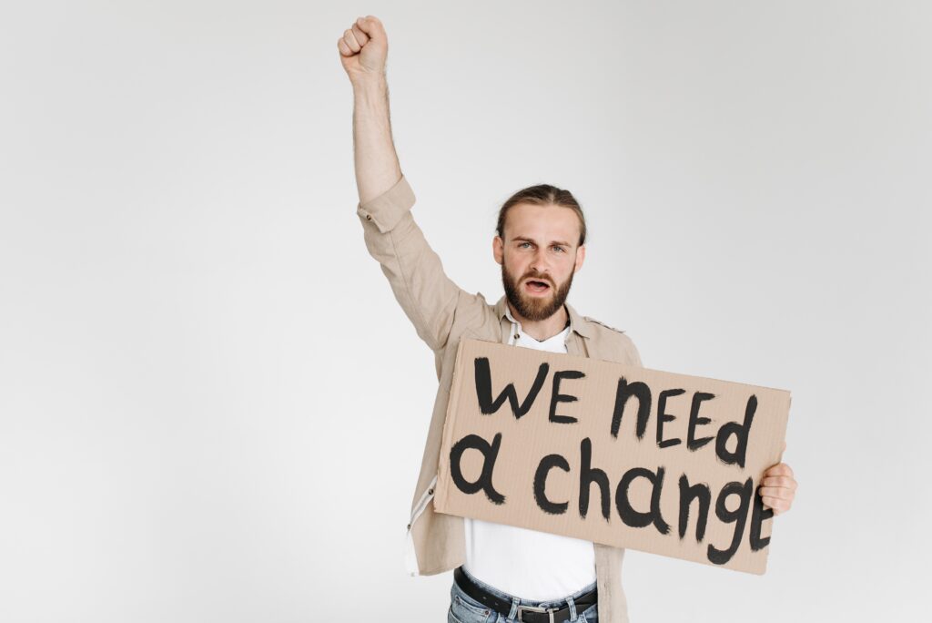 Homme blanc au poing levé tenant une pancarte sur laquelle on peut lire &quot;We need a change&quot; (Nous avons besoin d&#039;un changement).
