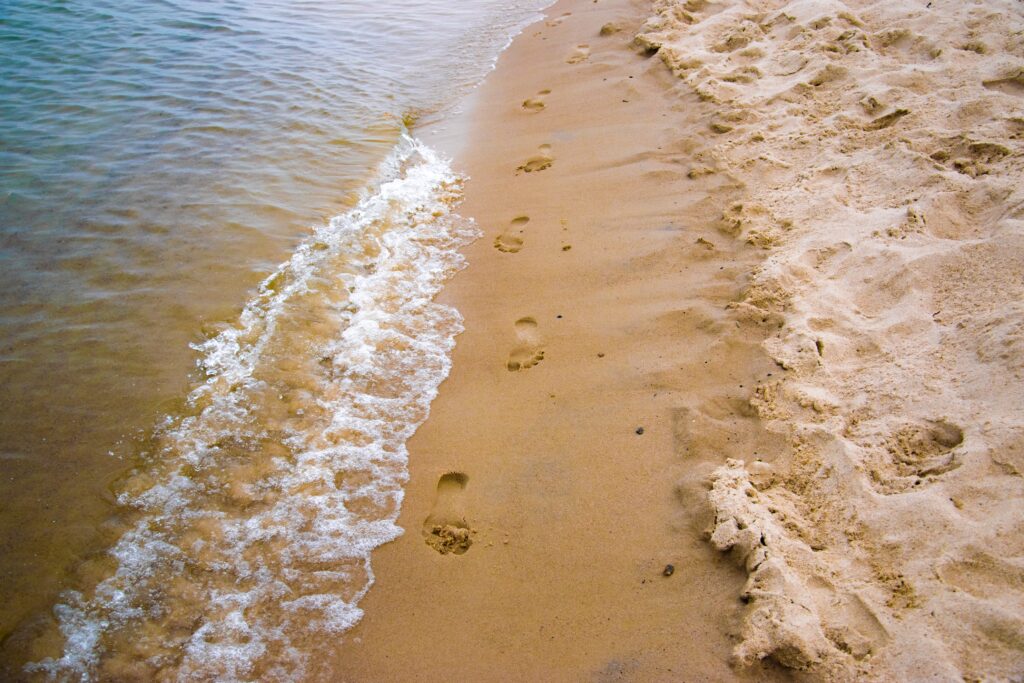 Shoreline of beach with footprints in the sand.