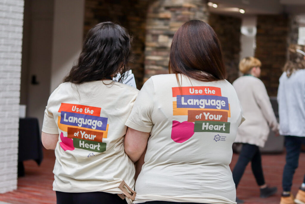 Two women standing with t-shirts that say, "Use the Language of Your Heart."